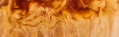 Preview: close up view of brown coffee mixing with milk in glass, panoramic shot