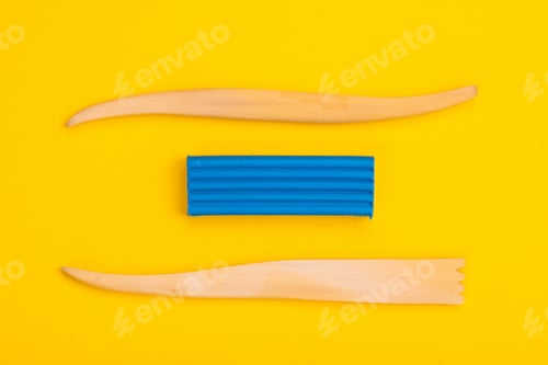 Preview: bar of blue plasticine and cutters lie isolated on a yellow background