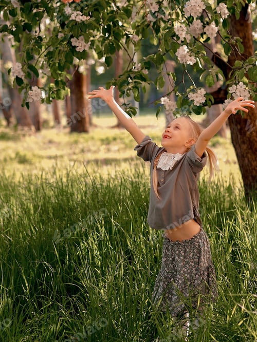 Preview: happy little girl with a smile walks in a flowering apple orchard in the country in spring (summer)