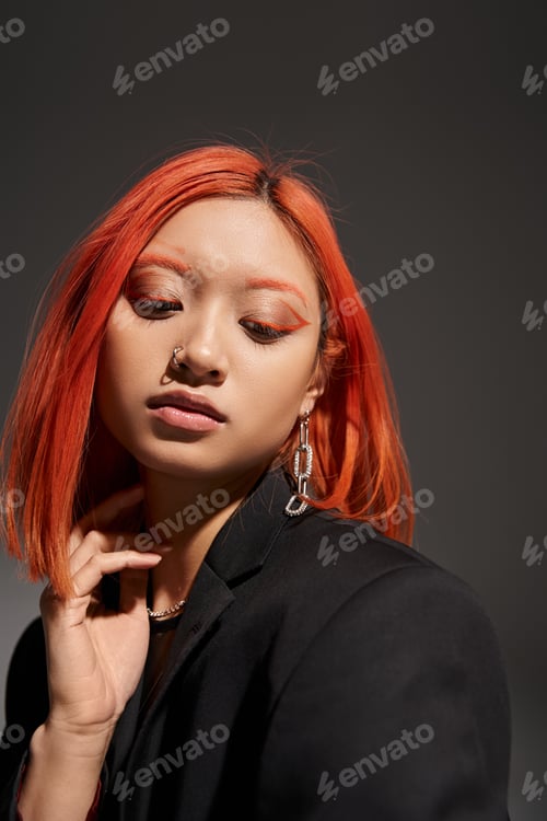 Preview: portrait of young asian woman with red hair, nose piercing and eye makeup posing on grey