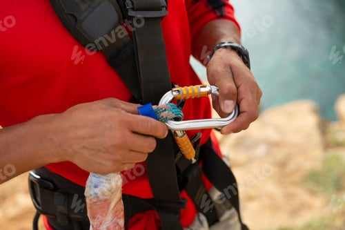 Preview: extreme athlete is preparing to jump off a cliff. Fastening the cable with carabiner. Insurance.