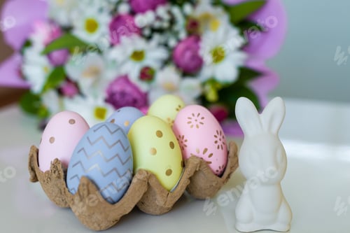Preview: Easter holiday multi-colored painted eggs and a white bunny rabbit, a bouquet of flowers in defocus