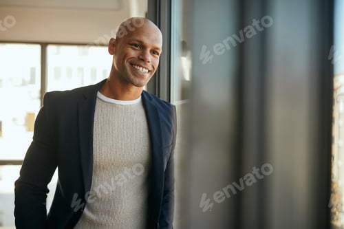 Preview: Happy black entrepreneur looking through the widow at his office.