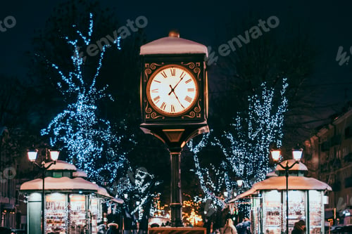 Preview: Antique clock in the city square. Christmas festive decorations on street.