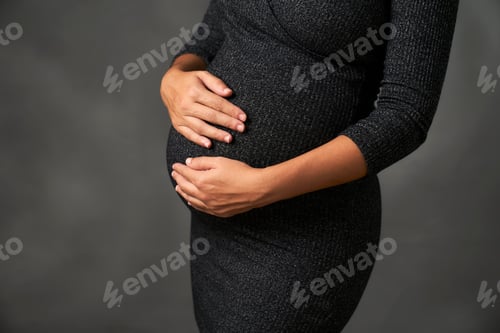 Preview: detail of hands touching the belly in profile view of a pregnant woman