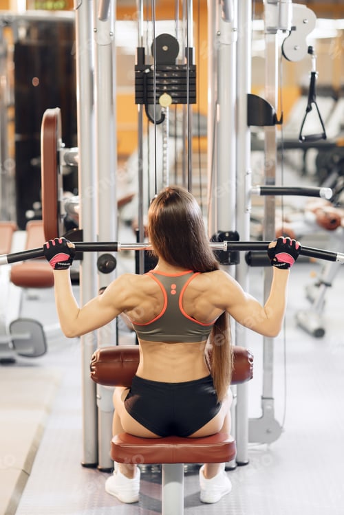 Preview: Young woman working at the lat pulldown machine in the gym,