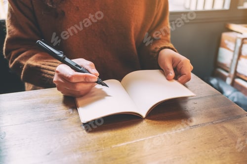 Preview: Closeup image of a woman writing on blank notebook with fountain pen on wooden table
