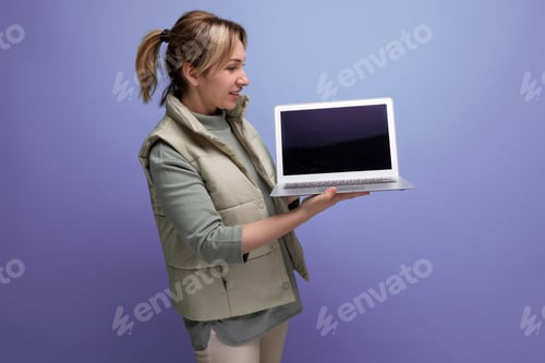Preview: blond millennial woman showing screen of laptop computer with mockup