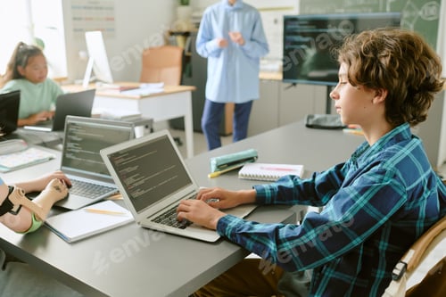 Preview: Teenage Caucasian Boy Coding on Laptop in Classroom with Diverse Students