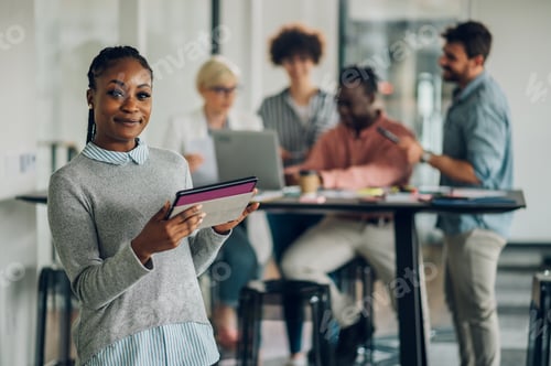 Preview: African american business woman standing in a office with colleagues in the back