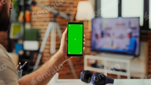 Preview: Young adult holding smartphone with green screen display