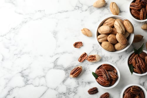 Preview: Flat lay composition with tasty pecan nuts on marble table. Space for text
