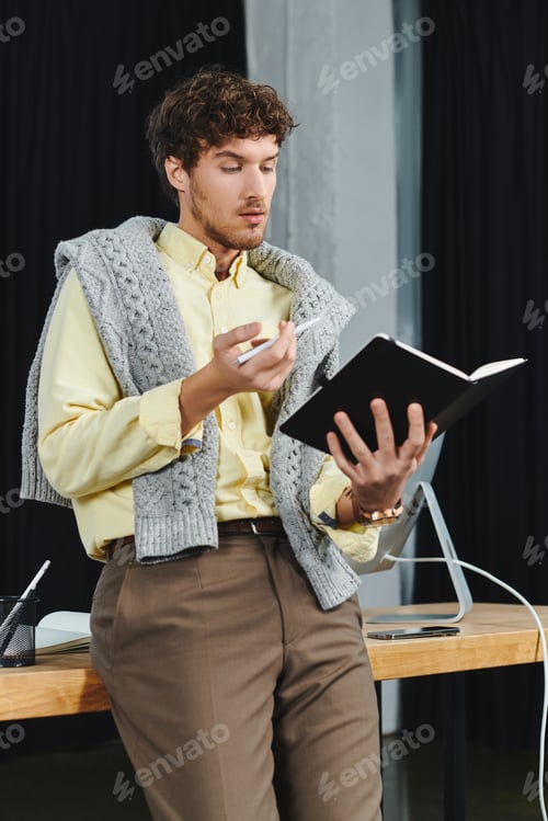 Preview: In a contemporary office environment, a young man reviews notes while standing casually.