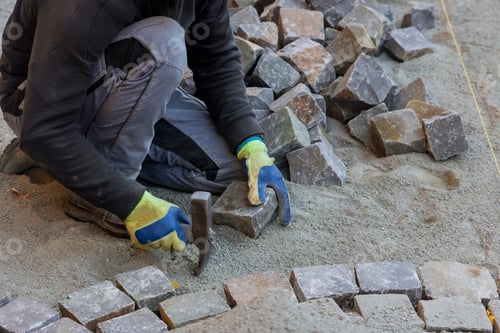 Preview: Road master in gloves lays paving stones in layers stone road by professional worker using stones