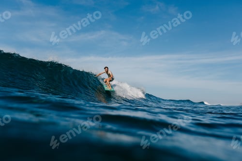 Preview: handsome man in wet t-shirt riding waves on surfboard