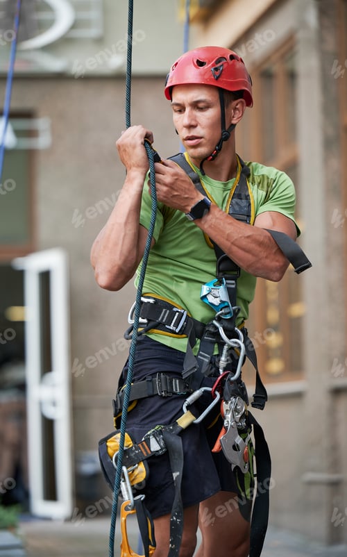 Preview: Industrial mountaineering worker cleaning window outside building.
