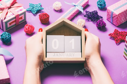 Preview: Top view of female hands holding calendar on purple background. The first of January