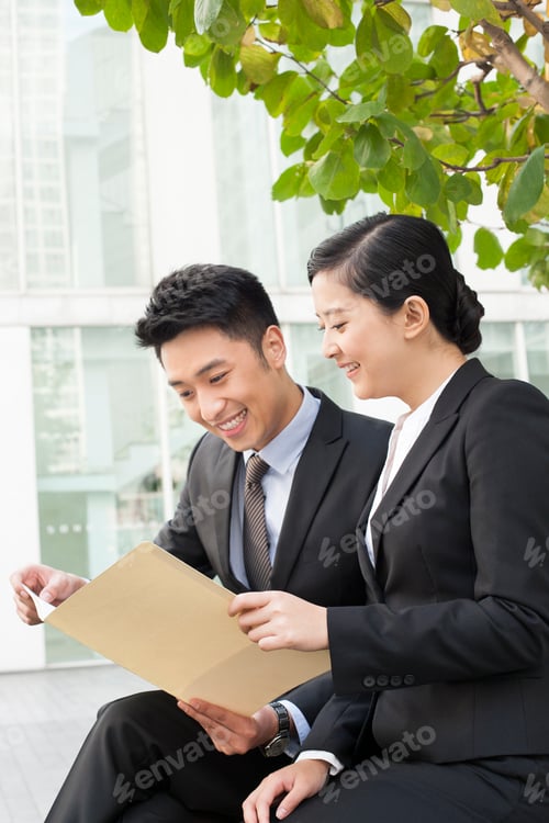 Preview: Happy young Chinese business partners studying a portfolio outdoors