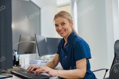 Preview: Nurse on Duty working on computer at the Reception Desk in modern clinic and looking camera