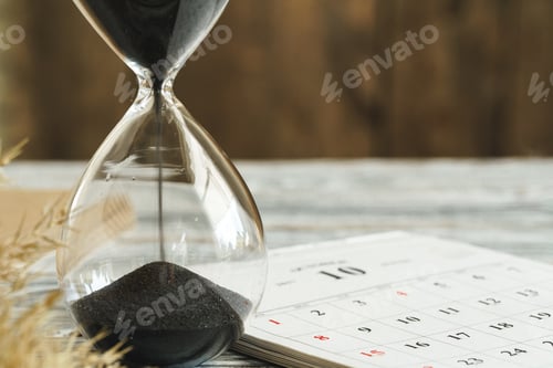 Preview: Hourglass with calendar on wooden desk close up