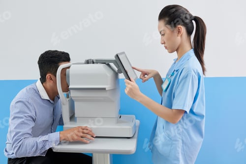Preview: Young female doctor setting refractometer machine to check eyes of patient before vision correction