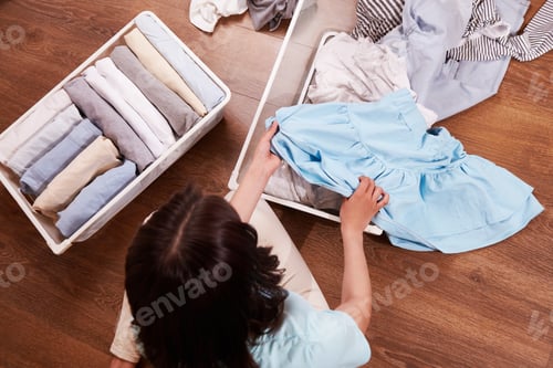 Preview: A young woman puts clothes in a metal laundry basket.