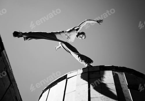 Preview: Young man jumping and practicing parkour between buildings roofs outside on clear summer day with