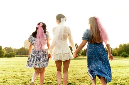 Preview: Happy charming bride in a white dress with a white veil and two bridesmaids with pink veils hugging