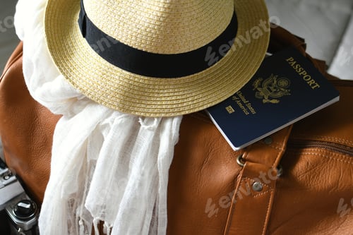 Preview: Packed summer vacation travel items. Brown leather bag with travel accessories sitting on a bed.