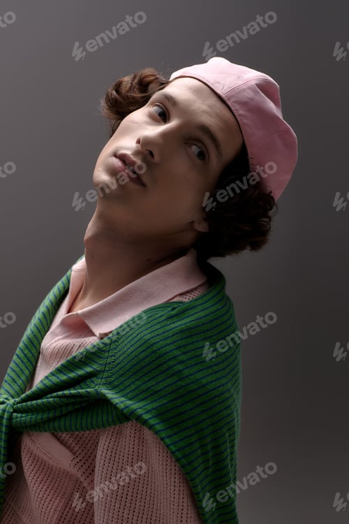 Preview: Stylish young man showcases unique fashion in modern grey studio setting