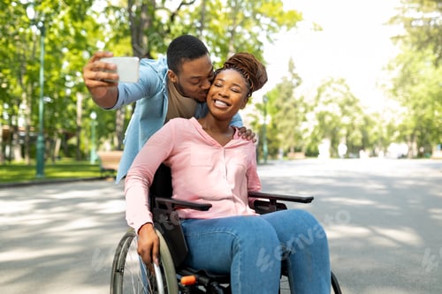 Preview: Romantic black man and his impaired girlfriend in wheelchair taking selfie together, kissing at city