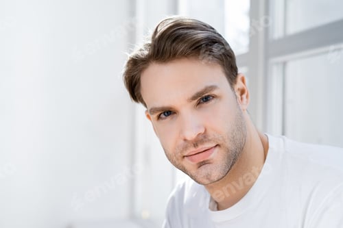 Preview: portrait of young man looking at camera near blurred window