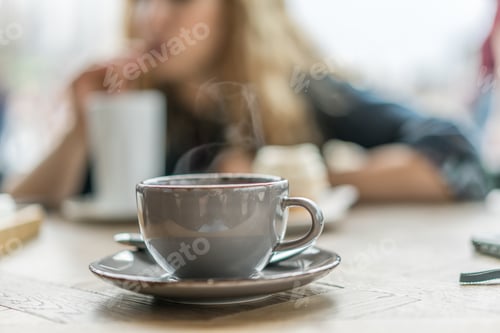 Preview: Coffee Cup on Table with Woman in Background