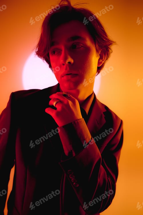 Preview: Young stylish man poses confidently against a warm glowing background at dusk