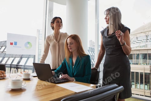 Preview: Three professionals discussing over a laptop in a modern office setting