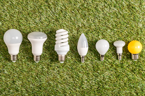 Preview: flat lay of fluorescent lamps on green grass, energy efficiency concept
