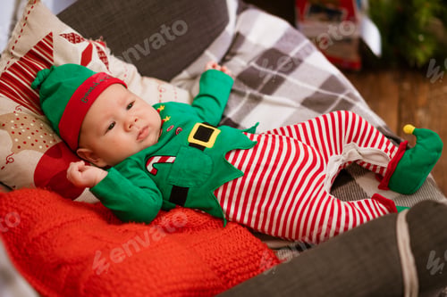 Preview: Christmas concept little boy cheerful elf looking up lies on multi-colored