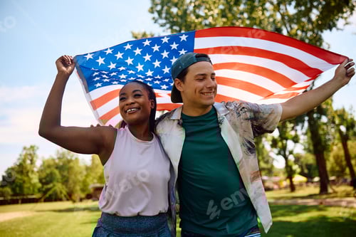 Preview: Happy multiracial couple holding American flag while walking in nature.