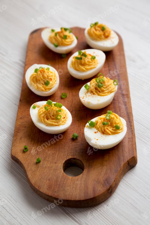 Preview: Homemade Deviled Eggs with Chives on a rustic wooden board on a white wooden table, side view.
