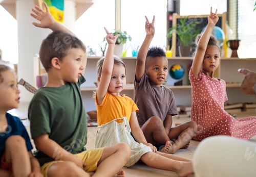 Preview: Group of small nursery school children sitting on floor indoors in classroom, raising hands