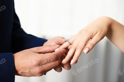Preview: Making proposal. Man putting engagement ring on his girlfriend's finger indoors, closeup