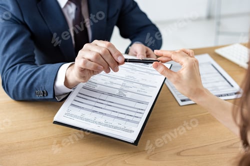 Preview: cropped view of car dealer giving pen to woman while holding clipboard with document