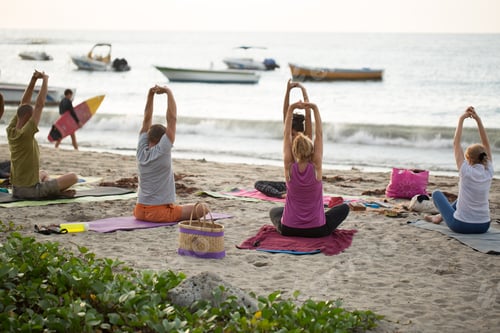 Preview: Women doing yoga exercises or supported pigeon pose on an empty beach