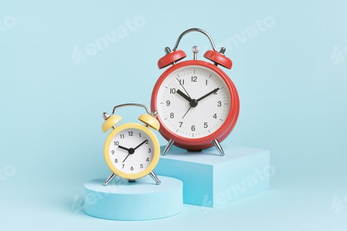 Preview: Yellow and red alarm clocks on podiums on a blue background.