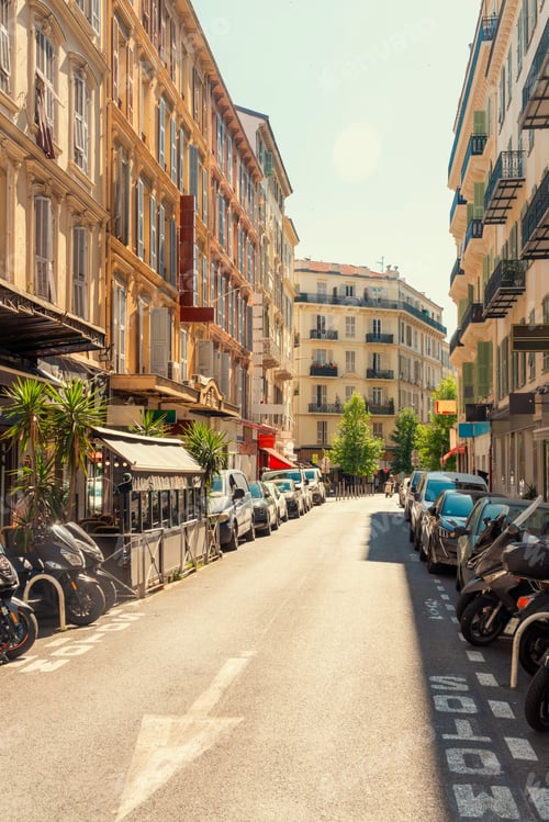 Preview: Sunny city street with outdoor cafe seating, lined with traditional European architecture