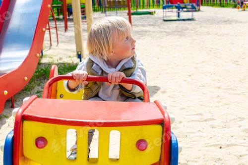 Preview: Cute blond little young toddler kid child boy sitting and riding in toy car,bus, train in playground