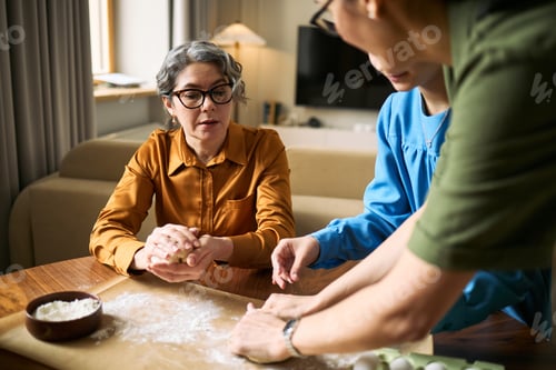 Preview: Senior Woman Teaching Family Baking Dough at Home Together