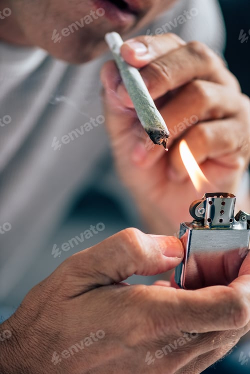 Preview: cropped view of man lighting up blunt with medical cannabis