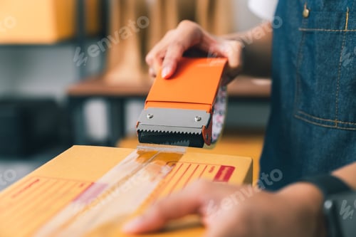 Preview: owner using adhesive tape, packing carton box working at the home office, prepares the delivery.