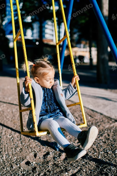 Preview: Little girl swinging on a swing holding on to the handrails